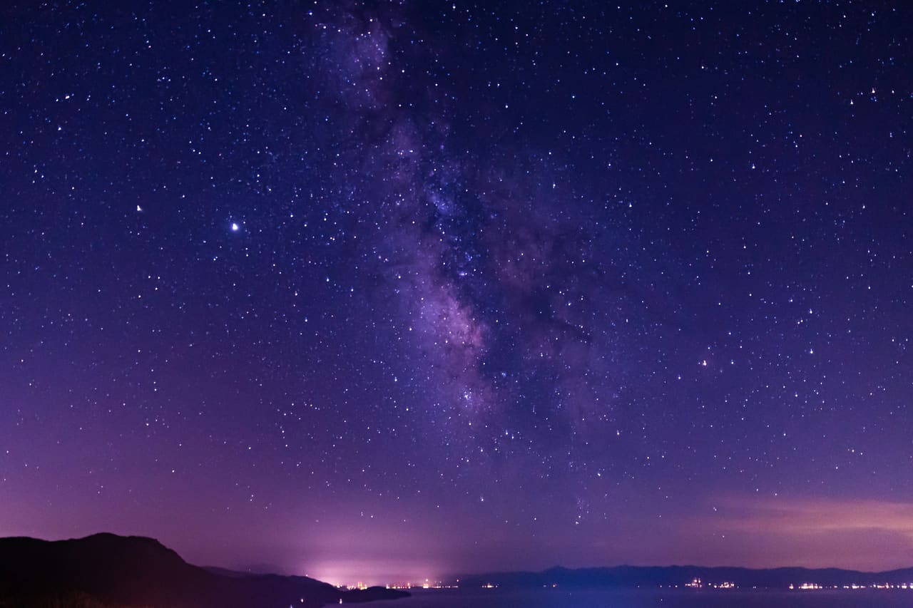 The Milky Way in a violet night sky above a dark mountain horizon