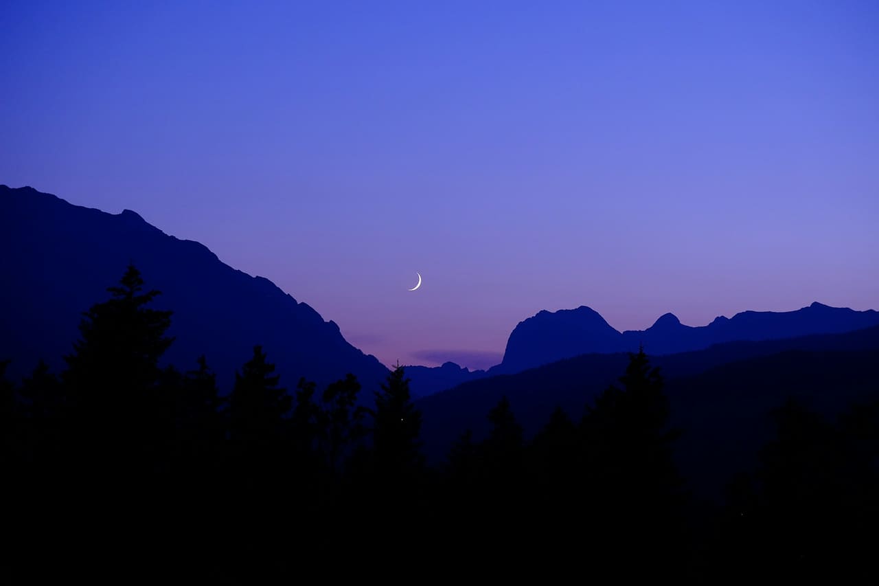 A thin crescent moon above mountain silhouettes at dusk